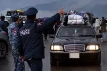 Ein schwarzes Auto mit viel Gepäck auf dem Dach fährt an zwei Polizisten vorbei, im Hintergrund viele Menschen und Autos, dahinter verregnete Berge