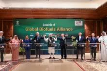 Mehrere Staatsoberhäupter (Joseph Biden, Lula da Silva, Cyril Ramaphosa, Sheikh Mohamed bin Zayed Al Nahyan, Narendra Modi, Justin Trudeau, Pravind Kumar Jugnauth, Lee Hsien Loong, Giorgia Meloni, and Sheikh Hasina) stehen in einem Halbkreis. Sie halten sich an den Händen recken diese triumphierend bis auf Schulterhöhe. Im Hintergrund steh ein grünes Banner mit der Aufschrift "Launch of Global Biofuels Alliance - G20 India"