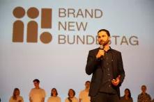 Maximilian Oehl steht vor dem Logo 'Brand New Bundestag' und spricht mit einem Mikrofon