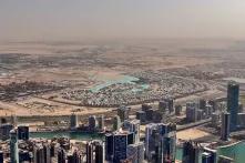 Blick aus Luft auf die Skyline von Dubai, dahinter sandige Böden und staubige Luft