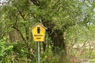 Ein gelbes Naturschutzgebiets-Schild steht vor einem Baum