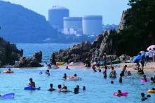 Menschen baden an einem Strand, im Hintergrund das Atomkraftwerk Fukushima