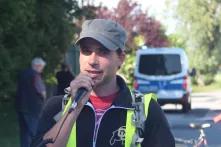  Fabian Czerwinski steht mit Warnweste und Mikrofon auf einer Straße, im Hintergrund steht ein Einsatzwagen der Polizei.