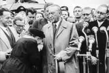 Flughafen Köln/Bonn.- Alte Frau küsst Konrad Adenauer die Hand; rechts: Bundesaußenminister Heinrich von Brentano
