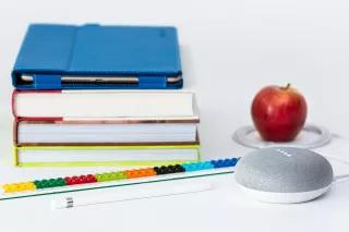 Ein Tablet auf einem Bücherstapel, daneben ein Apfel und ein Lautsprecher
