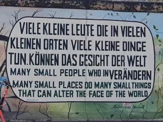Graffiti auf Mauer mit Spruch: Viele kleine Leute die in vielen kleinen Orten viele kleine Dinge tun können das Gesicht dere Welt verändern - Deutsch und Englisch in großen Lettern