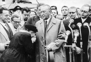 Flughafen Köln/Bonn.- Alte Frau küsst Konrad Adenauer die Hand; rechts: Bundesaußenminister Heinrich von Brentano